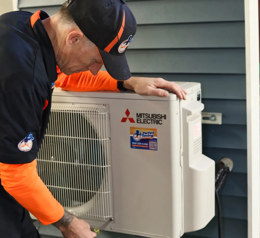 Perfect Timing Heating & Cooling technician performing heat pump maintenance on a Mitsubishi Electric heat pump system to ensure reliable year-round comfort